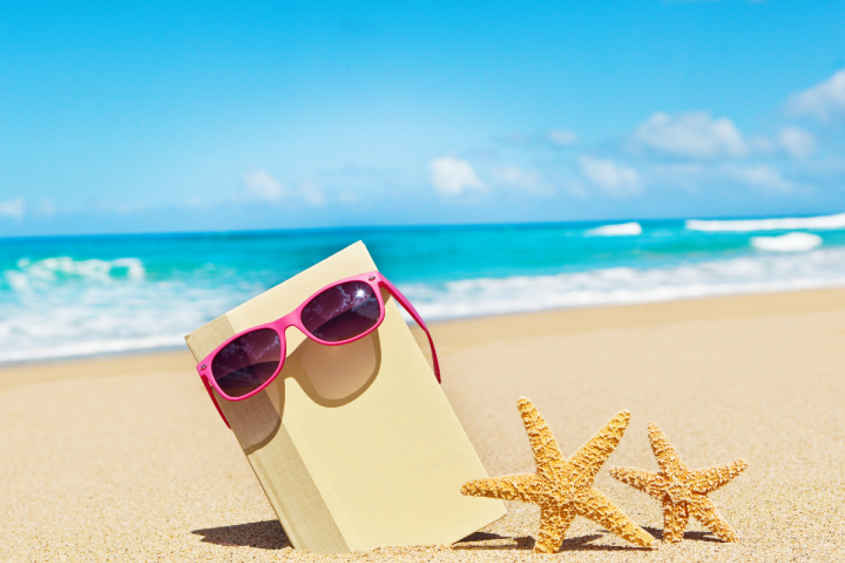 Photo of a book wearing sunglasses on the beach next to two starfish